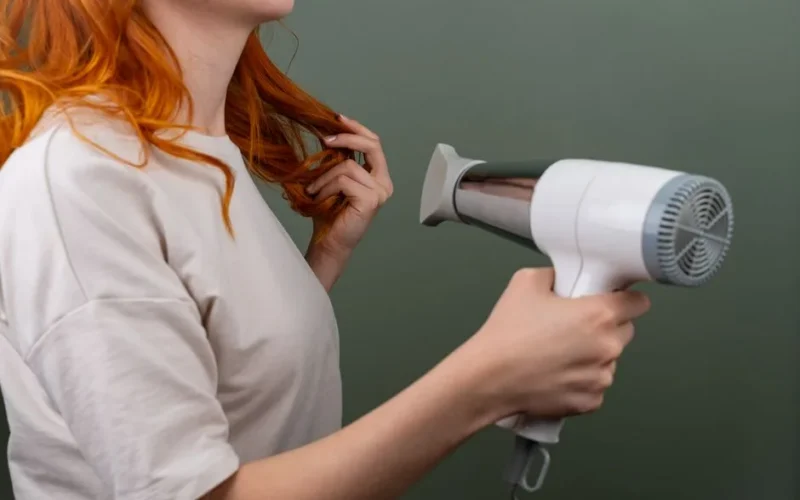 Woman blow drying her vibrant red hair with a modern blow dryer, showcasing hair styling technique.