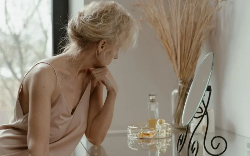 Senior woman with blonde hair looking in mirror, reflecting on beauty and aging gracefully.