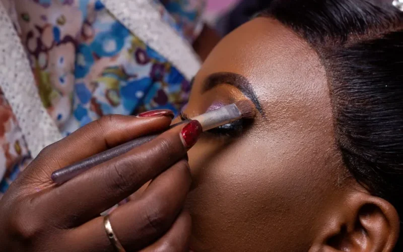 Close-up image of a makeup artist applying eyeshadow to a woman's eyelid, highlighting beauty and fashion.