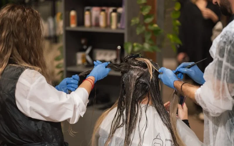 Professional stylists dyeing a woman's hair in a modern salon setting, showcasing teamwork and expertise.