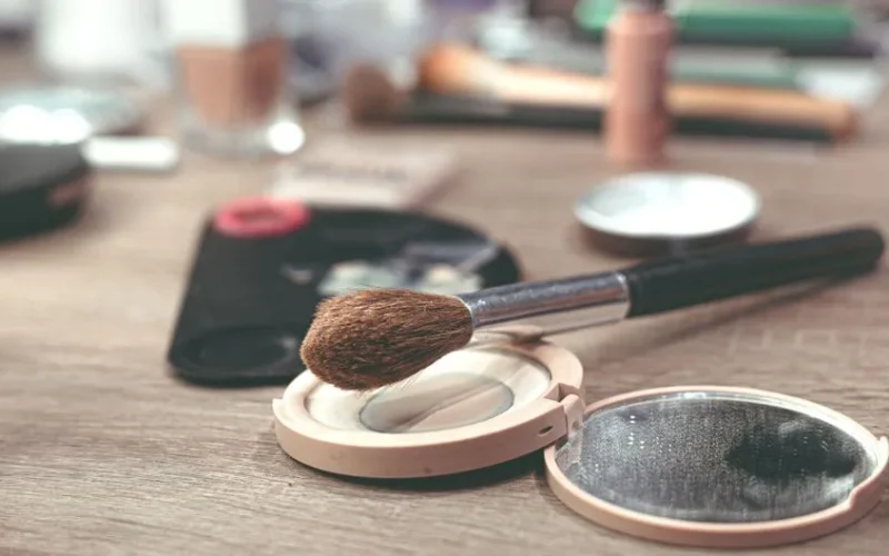 Close-up image of makeup brushes and compact powder on a wooden surface, ideal for beauty themes.