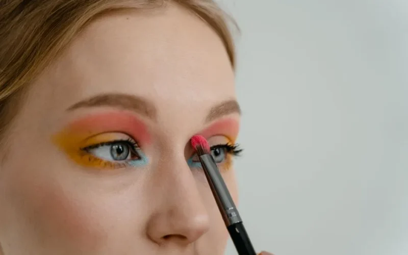 Vibrant eyeshadow application close-up with makeup brush on woman's eyelid.