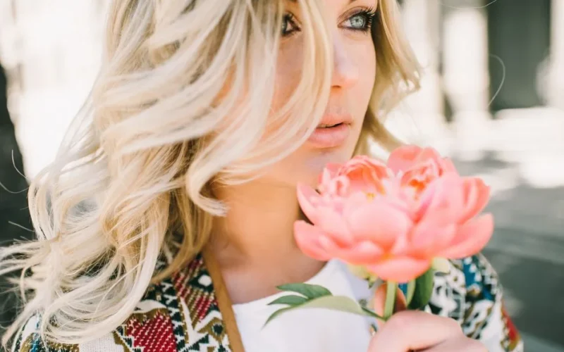 Close-up of a blonde woman holding a pink flower, showcasing beauty and nature.
