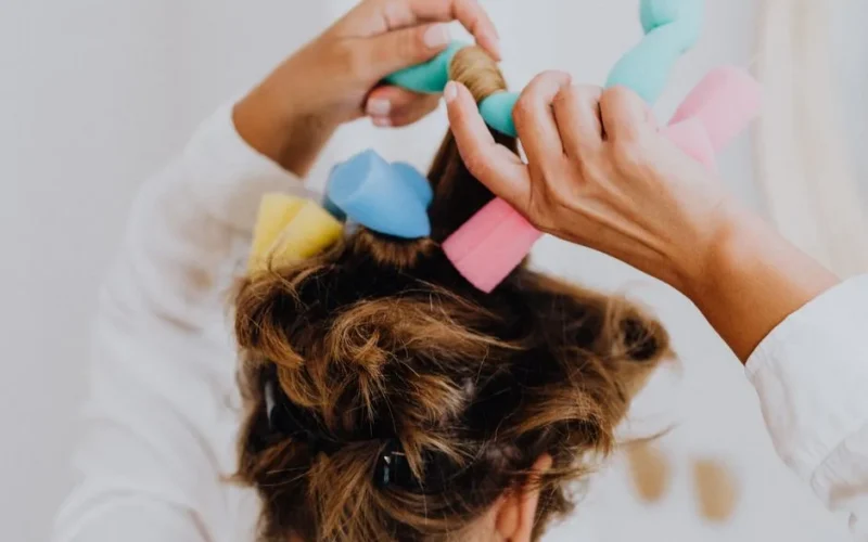 Woman styling hair with soft foam curlers in a close-up view.