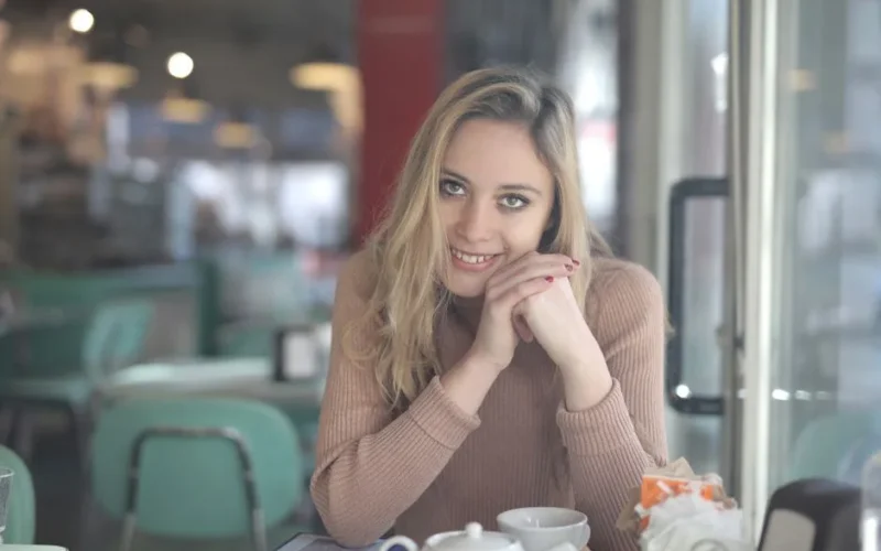 A cheerful woman in a cozy café, enjoying a relaxed moment with a smile.