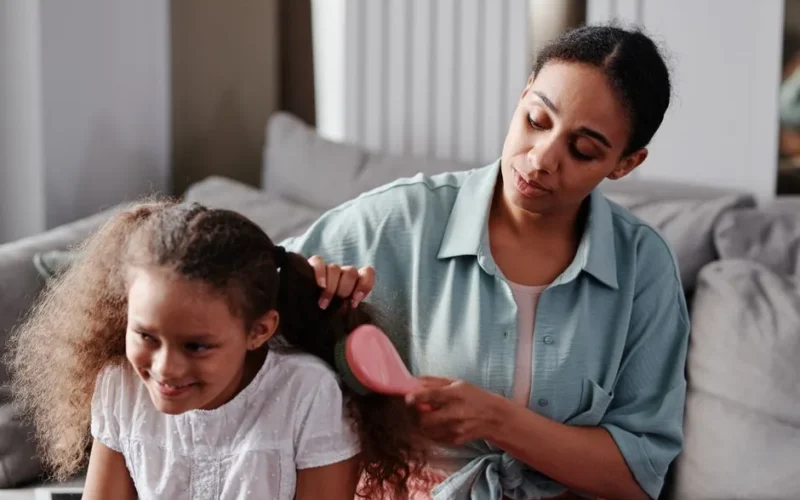 A mother gently brushes her daughter's hair on a couch, illustrating tender family moments.