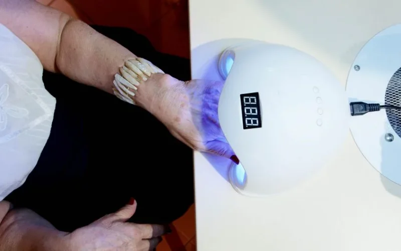 Close-up of a woman's hand with a bracelet using a nail dryer in a salon setting.
