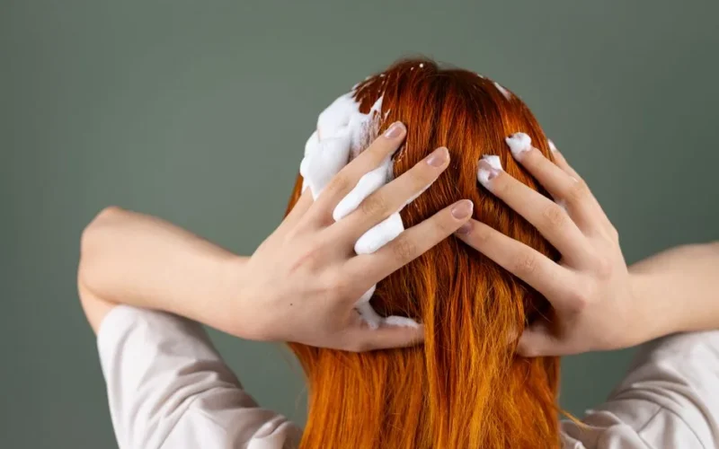 Back view of person washing red hair with shampoo in studio setting.