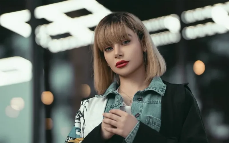 Portrait of a stylish woman with blonde hair and denim jacket at night.