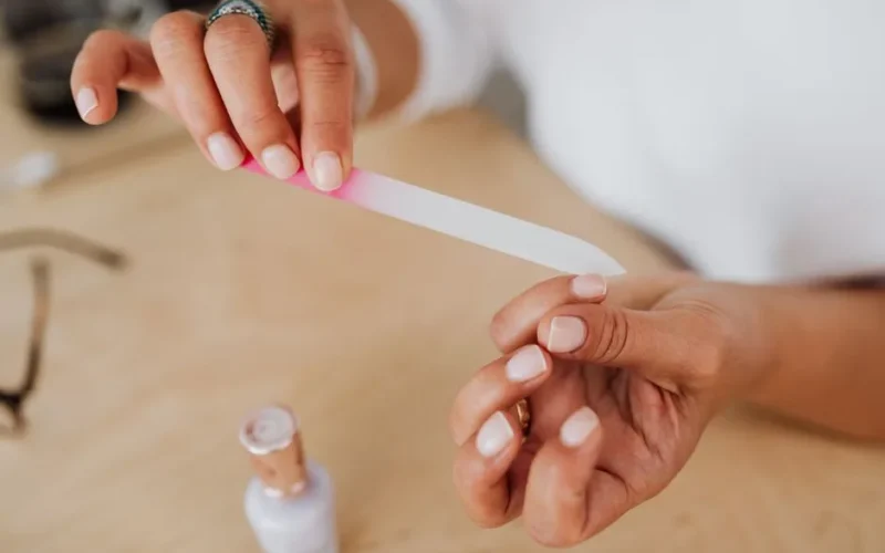 Detailed view of hands filing nails with a nail polish bottle nearby, showcasing personal grooming.