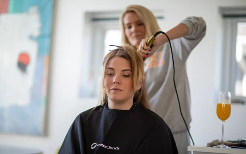 A woman gets her hair styled with a curling iron in a contemporary salon setting.