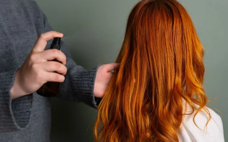 Close-up of hairdresser spraying hair product on long red hair.