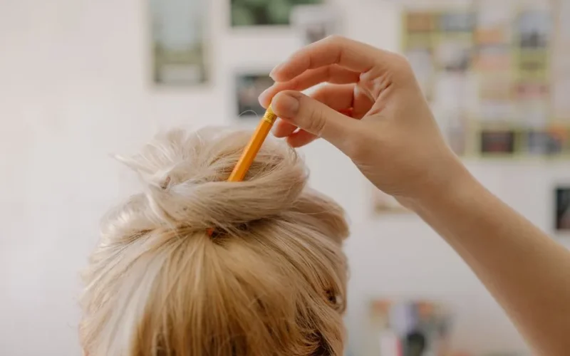 Close-up of a blonde hairstyle with a pencil used as a hair accessory, creating a stylish bun look.