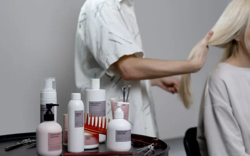 A hairdresser styling a blonde woman's hair in a salon, showcasing hair care products on a table.
