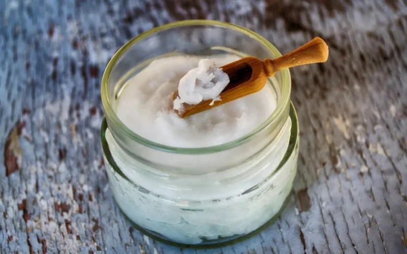Close-up of organic coconut oil in glass jar with wooden spoon, perfect for natural health and wellness use.