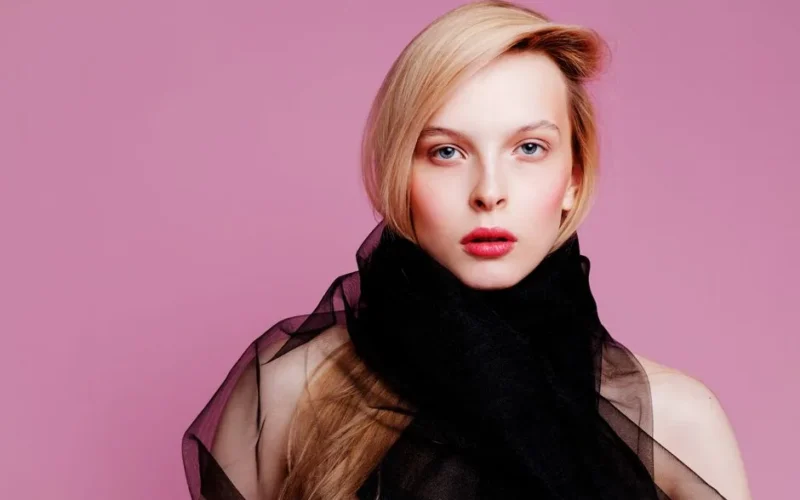 Striking portrait of a woman with blonde hair and red lips against a pink background.
