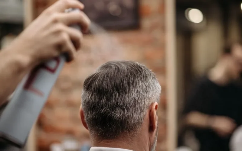 A professional barber styles a man's hair with hairspray in an urban barbershop.