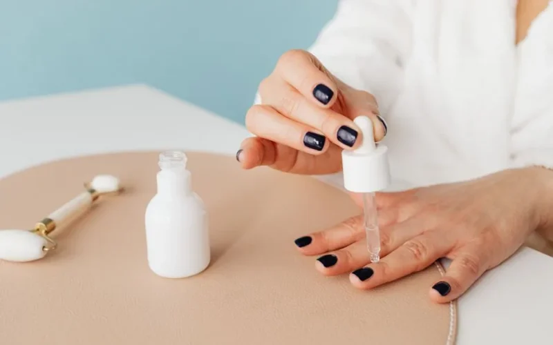 Close-up of a woman applying nail oil with a dropper for manicure care on blue background.