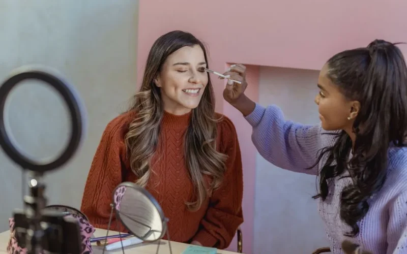 African American makeup artist applying eyeshadow on eyelid while recording beauty blog on smartphone on tripod