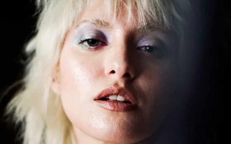Artistic close-up portrait of a woman with blonde hair and vivid makeup, captured in moody lighting.