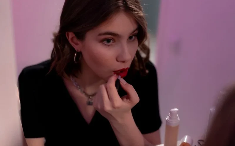 A young woman applies lipstick in front of a mirror, focusing on her makeup routine.