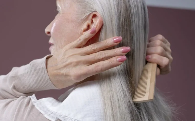 Elderly woman with silver hair combing her hair, highlighting graceful aging and care.