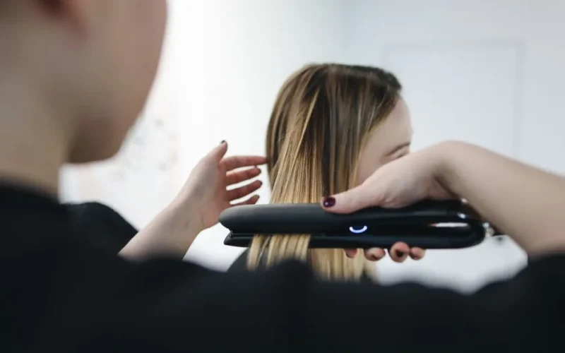 Close-up of a hairstylist using a straightening iron for sleek hairstyle indoors.