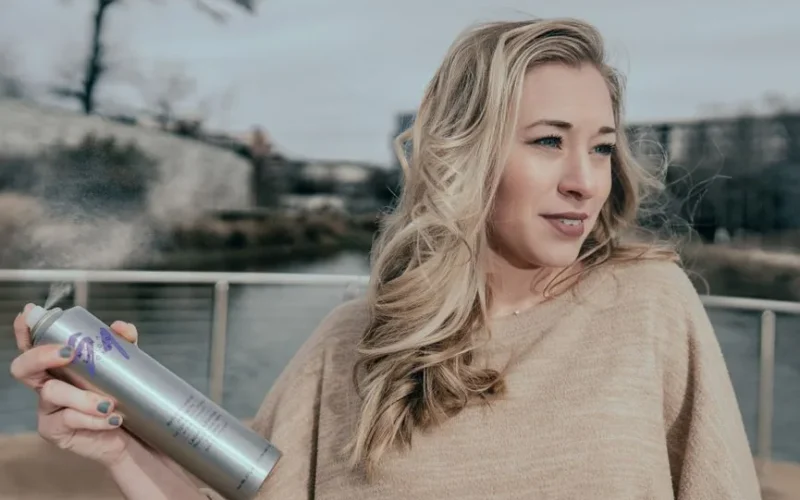Blonde woman holding hair spray outdoors in Atlanta, Georgia, showcasing styling action.