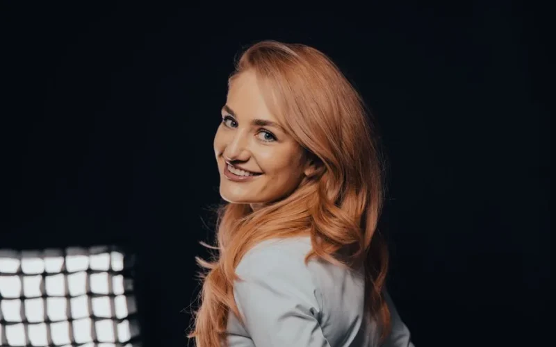 Smiling woman with long blonde hair posing against a dark background in a professional studio setting.
