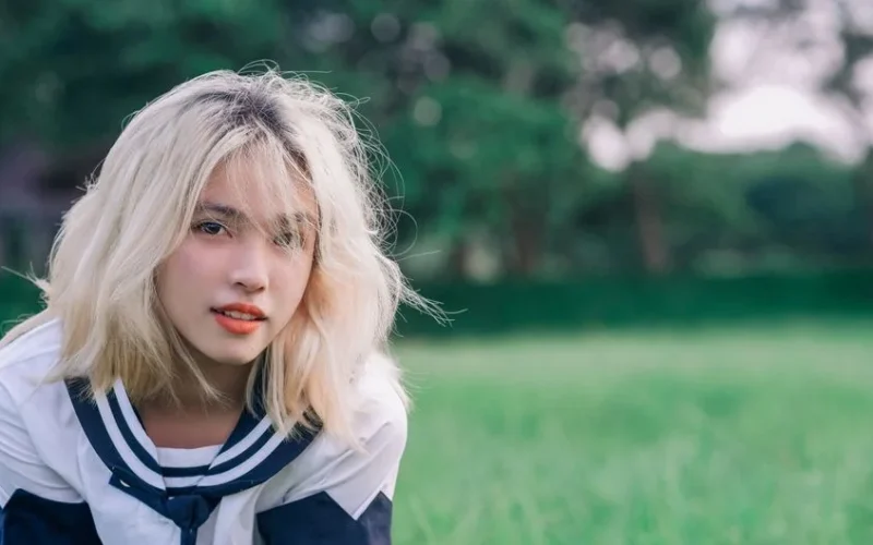 A young woman with blonde hair poses outdoors on a summer day.