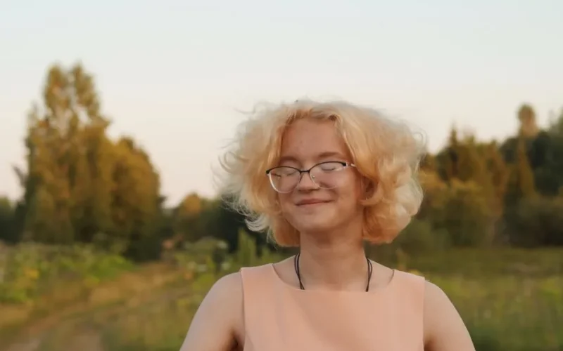 Portrait of a smiling woman with beautiful blonde hair in a serene outdoor setting.