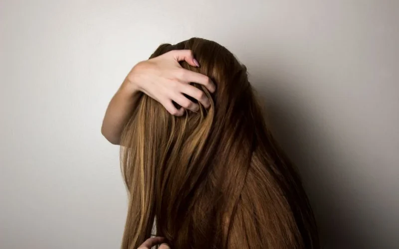 An artistic close-up of a woman's long brunette hair held gently by her hand, emphasizing texture and color.