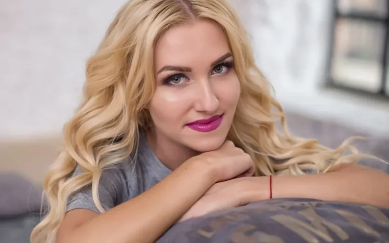 Portrait of a blonde woman with glamorous makeup relaxing indoors with a serene smile.