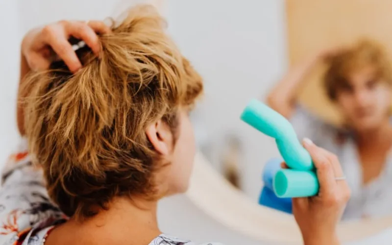 Woman using blue curlers in front of a mirror for daily hair routine.