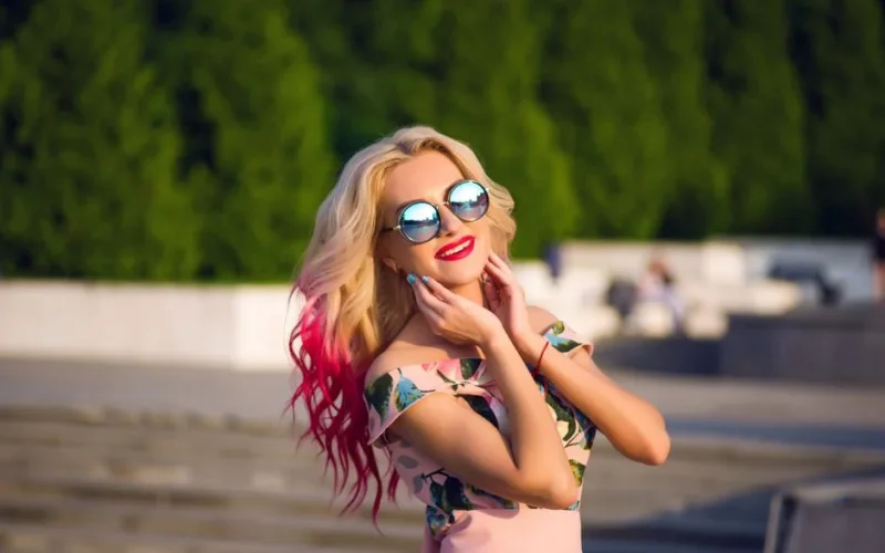 A fashionable woman with pink-tipped hair and sunglasses enjoying a sunny summer day outdoors.