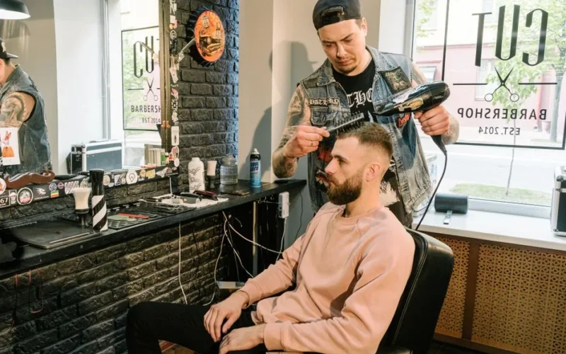 Barber styling a man's hair with a blow dryer in a contemporary barbershop setting.